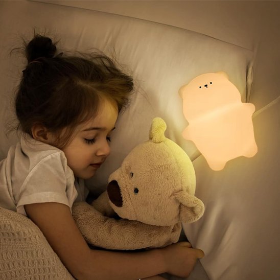 Bebe veilleuse | Douceur Tactile encore allumée posée sur l'oreiller sur laquelle une fillette est endormie avec son ourson en peluche entre les bras.