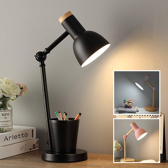 Lampe de chevet articulée noire. L'abat-jour est noir et le dessus de couleur bois. Il y a un porte-crayons noir sur sa base. Elle est placée sur un bureau, deux livres sont déposés un par dessus l'autre et il y a un pot contenant des fleurs par dessus. Deux encarts présentent la lampe avec la base et le bras de couleur bois. L'abat-jour d'une des lampes est rose, l'autre blanc. Le dessus des abat-jours est couleur bois.