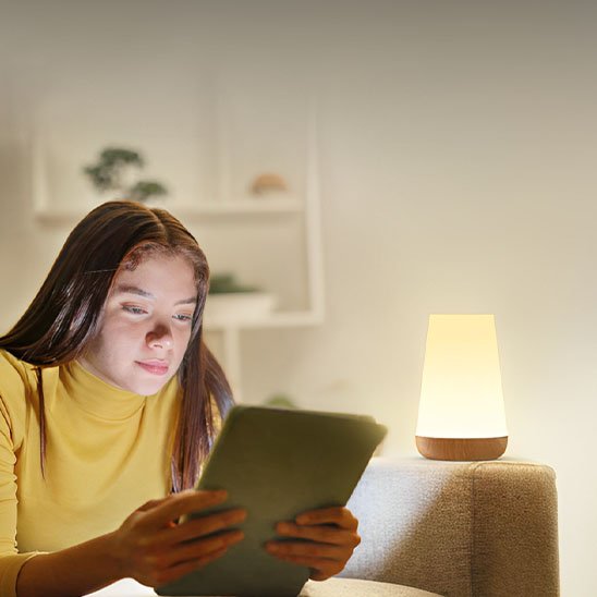 On voit une adolescente qui étudie avec la Lampe de chevet tactile | LumiTouch comme lampe de lecture.