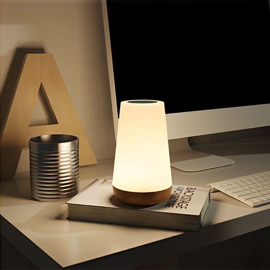 On voit la Lampe de chevet tactile | LumiTouch comme éclairage d'espace de travail. Elle est déposée par dessus un livre à côté d'un clavier et d'un écran.