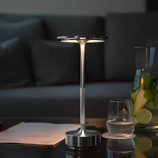 L'image montre la lampe de table | ModernTouch sur une table à café du Living-Rom et sur cette table sont posées un document, un verre à moitié et une cruche d'eau citronnée.