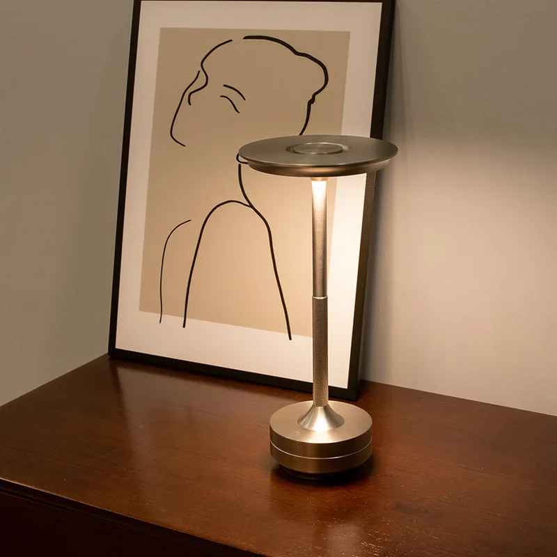 Lampe MoedernTouch de couleur or posée sur un meuble sur lequel un cadre est présent appuyé sur un mur