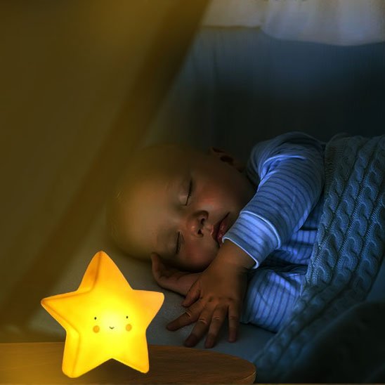 Une veilleuse bébé | Étoile Douce Nuit de couleur Jaune posée sur une table de chevet éclaire un bébé endormi