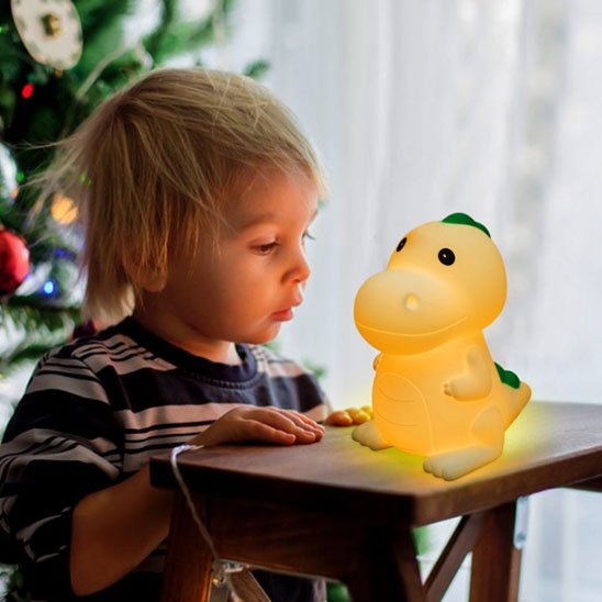 Un enfant regarde la veilleuse bébé | dinosaure DinoNuit posée sur un escabeau devant lui