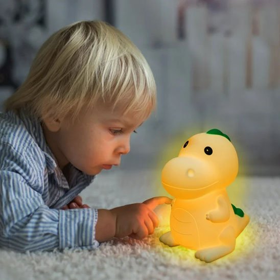 Un enfant coucher au sol sur le ventre touche la veilleuse bébé | dinosaure DinoNuit devant lui