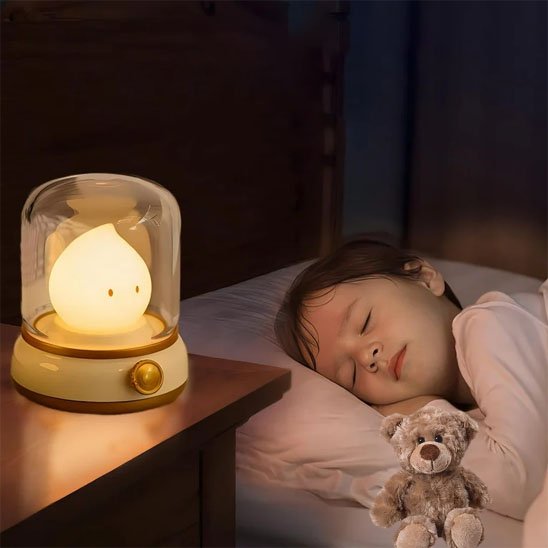 La veilleuse bébé | Goutte-Apaisante de couleur jaune, est posée sur la table de chevet d'un enfant endormi avec son doudou
