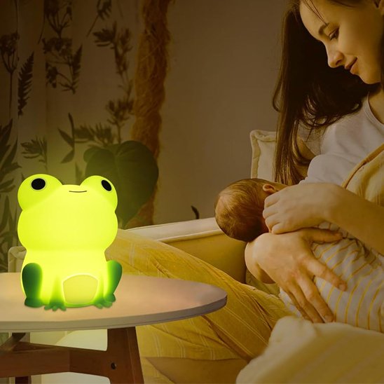 Un maman allaite son bébé. Ils sont éclairés par la veilleuse bébé | Grenouille Lumina posée sur une petite table