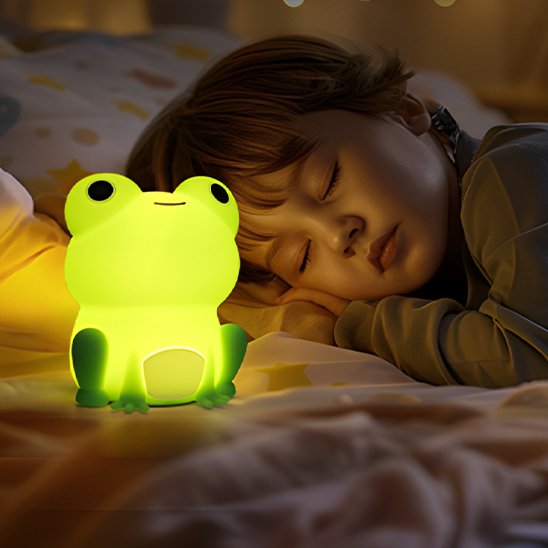 Un enfant dort avec la veilleuse bébé | Grenouille Lumina posée sur son lit