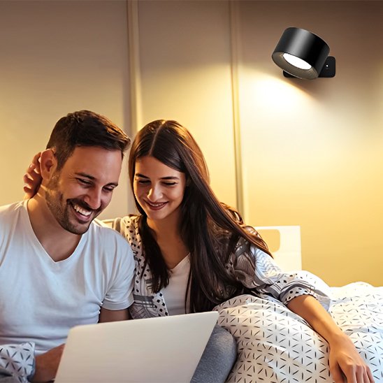 On voit un couple au lit qui regarde un ordinateur portable éclairés par l'applique murale chambre | Design Luminescence