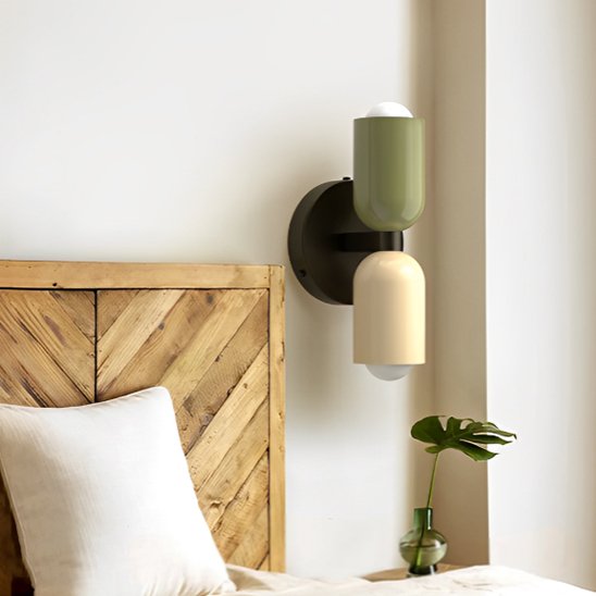 On voit une applique murale chambre | Design Ajustable l'abat-jour du haut est vert, celui du bas est blanc et le châssis noir. L'applique est installé au-dessus d'une table de chevet sur le mur blanc