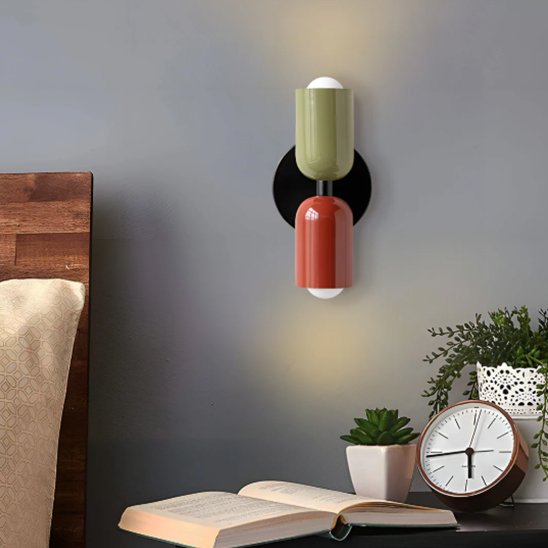 On voit une applique murale chambre | Design Ajustable l'abat-jour du haut est vert, celui du bas est prune et le châssis noir. L'applique est installé au-dessus d'une table de chevet sur le mur bleu acier