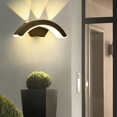 On voit l'applique murale pour extérieur | Elégance installée sur un mur près de l'entrée qui éclaire un arbuste rond dans une haute jardinière carré.