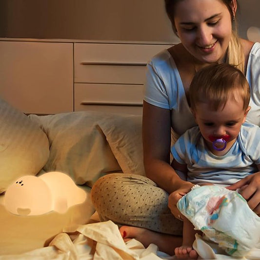 Bebe veilleuse | Douceur Tactile allumée sur un lit alors que maman est assise avec son bébé qui regarde sa couche tenu par sa maman