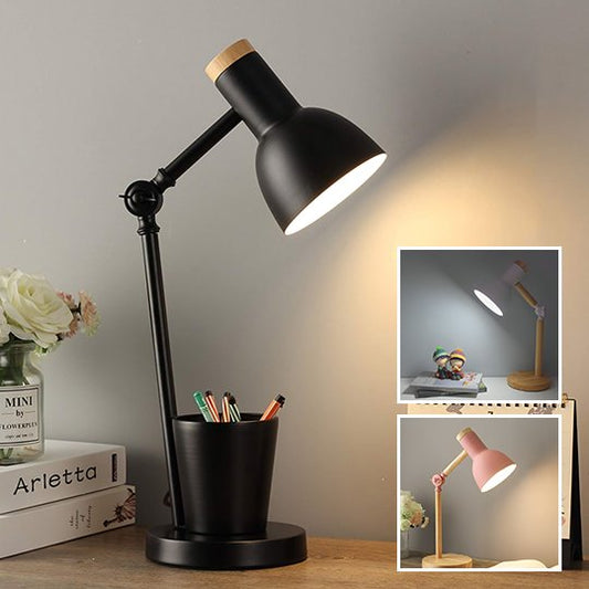 Lampe de chevet articulée noire. L'abat-jour est noir et le dessus de couleur bois. Il y a un porte-crayons noir sur sa base. Elle est placée sur un bureau, deux livres sont déposés un par dessus l'autre et il y a un pot contenant des fleurs par dessus. Deux encarts présentent la lampe avec la base et le bras de couleur bois. L'abat-jour d'une des lampes est rose, l'autre blanc. Le dessus des abat-jours est couleur bois. 