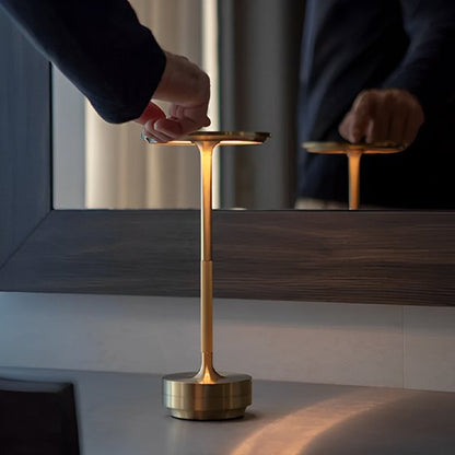 L'image montre une main d'homme qui appuie sur le dessus de la Lampe MoedernTouch de couleur or posée sur table devant un miroir dans lequel on voit le reflet de l'homme.