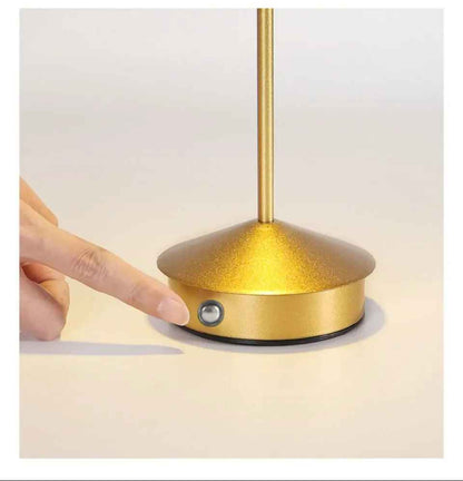 On voit un doigt qui s'apprête à appuyer sur l'interrupteur de la Lampe de table | Scandinave Or situé sur le côté de sa base 