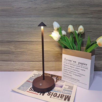L'image montre la Lampe de table Scandinave sur un journal près d'un sac en papier contenant des tulipes.
