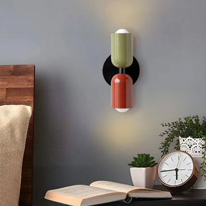 On voit une applique murale chambre | Design Ajustable l'abat-jour du haut est vert, celui du bas est prune et le châssis noir. L'applique est installé  au-dessus d'une table de chevet  sur le mur bleu acier