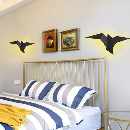 On voit deux appliques murales chambre | Design Cosy de couleur noire installées au mur de chaque côté d'une tête de lit en barres de métal métal dorée. Les appliques ont la forme d'un oiseau en pliage origami.  