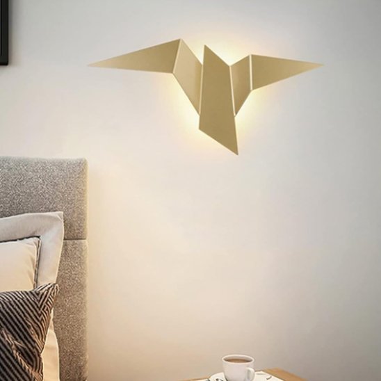 On voit une applique murale chambre | Design Cozy de couleur or installée au mur près d'une tête de lit grise.