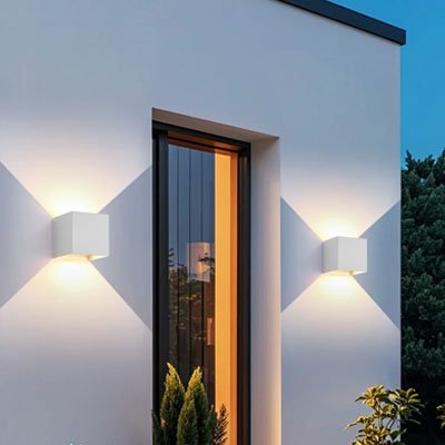 On voit deux appliques murales pour extérieur | Luminesence : de 6 ou 12 watts installée de chaque côté d'une porte vitrée. Elle est de forme cubique blanche  10 cm large par 10 cm haut et 10 cm profond, Diffuse la projection de la lumière vers le haut et le bas. 