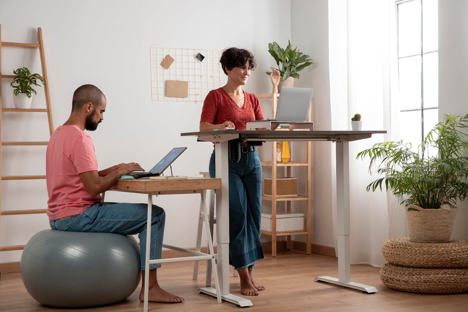 Un couple en télétravail. L'homme est assis sur un ballon d'exercices et la femme est debout prêt de sa table de travail assis-debout